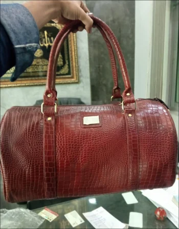 Make a lasting impression on your short getaways with the Classic Leather Overnight Travel Duffle. Crafted from rich, textured mahogany leather with reinforced perimeter stitching, this bag delivers a sophisticated vintage aesthetic while offering modern functionality for weekend getaways, gym sessions, or business travel. Key Features: Quick-Access Storage: Outfitted with a spacious front compartment secured by a polished metallic push-lock latch for keeping essentials like passports, keys, and wallets safe yet accessible. Comfortable Carrying: Designed with rolled leather double top handles fastened with sturdy metallic hardware, ensuring a comfortable grip whether carried by hand or over the shoulder. Protected Base: Equipped with heavy-duty bottom studs to shield the leather base from dirt, scuffs, and wear when placed on floors or luggage racks. Refined Finish: Showcases a smooth rounded silhouette, top double-zipper closure, and a sleek metallic accent plate for an executive finish. Specifications: Material: Textured Leather / Faux Leather Color: Rich Mahogany / Chestnut Brown Closure Type: Top Zipper Main Access & Metallic Push-Lock Front Pocket Hardware: Silver-Tone Metal Buckles & Accents